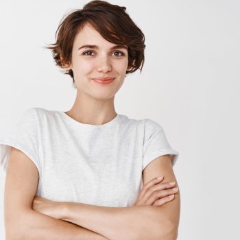 Portrait of confident and happy woman with short hair, cross arms on chest like professional and smiling, standing against white background.